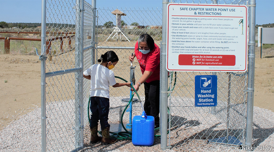 An indigenous woman and child collect water at a well.